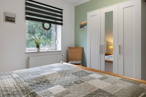 Une chambre à coucher avec un lit, une fenêtre donnant sur un paysage verdoyant, un fauteuil en osier et une armoire.