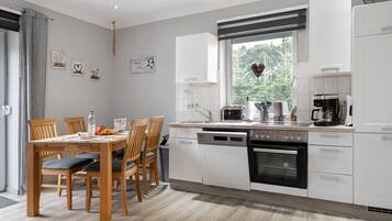 Une cuisine moderne avec des meubles blancs, un lave-vaisselle, un four et une machine à café.