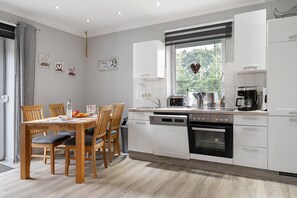 Une cuisine moderne avec des meubles blancs, un lave-vaisselle, un four et une machine à café.