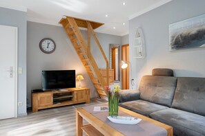 Un salon comprenant un meuble TV en bois, un canapé, une table basse avec un vase, une échelle en bois et une horloge murale.