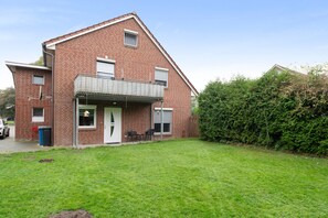 Ein zweistöckiges Backsteinhäuschen mit Veranda und kleinem Balkon, umgeben von einem gepflegten Rasen.