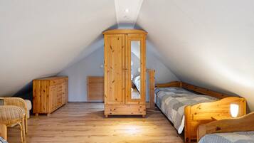 A small attic bedroom with a sloped ceiling, wooden wardrobe, two single beds, a wicker chair, and a small bedside table.