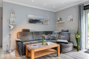 Un salon moderne avec un canapé gris, une table basse en bois et un tableau représentant une scène de plage.