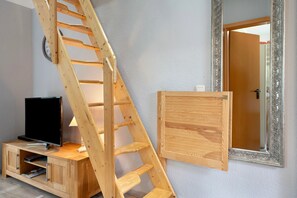 Ein Zimmer mit einer Holzleiter, einem Fernseher auf einem Holzschrank und einer Tür mit einem verzierten Spiegel.