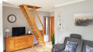 En stue med en trætrappe, et fjernsyn, et skab, en sofa, et ur og et billede i ramme på væggen.