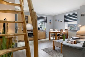 Une cuisine moderne avec des meubles en bois, un coin repas comprenant une table et des chaises, un canapé et une vue sur l’extérieur grâce à de grandes fenêtres.