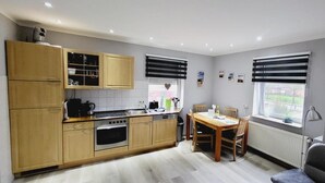 A compact kitchen with wooden cabinets, a dining table, and a window with blinds.