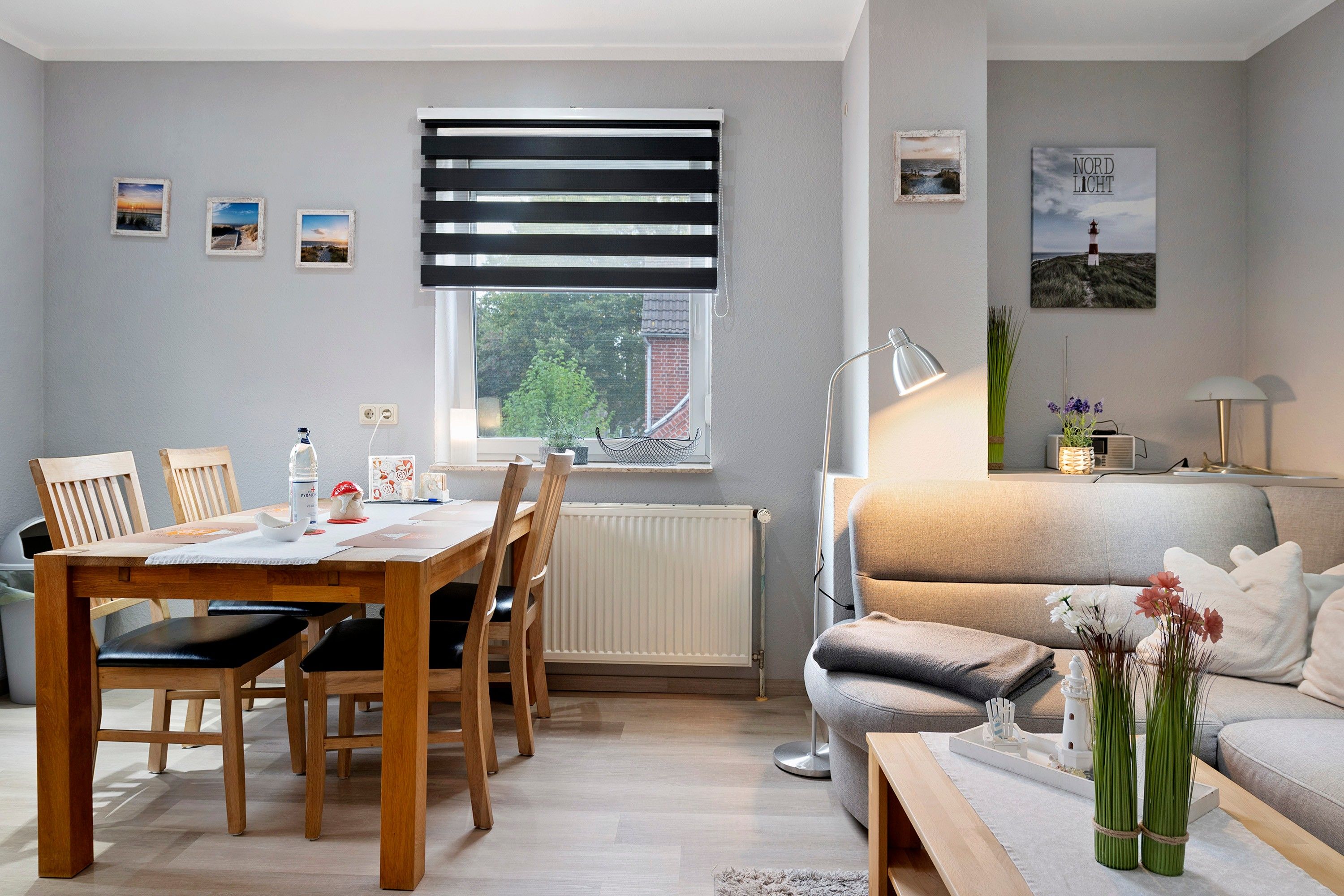 Ein gemütliches Wohnzimmer mit einer Couch, einem Esstisch mit Stühlen, einem Fenster mit Jalousien und einer Lampe.