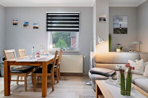 Een gezellige woonkamer met een bank, een eettafel met stoelen, een raam met jaloezieën en een lamp.