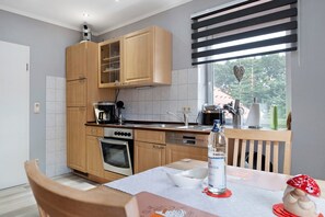 Eine moderne Küche mit Holzausstattung, einem Einbauofen, einer Kaffeemaschine und einem Fenster mit Jalousien.