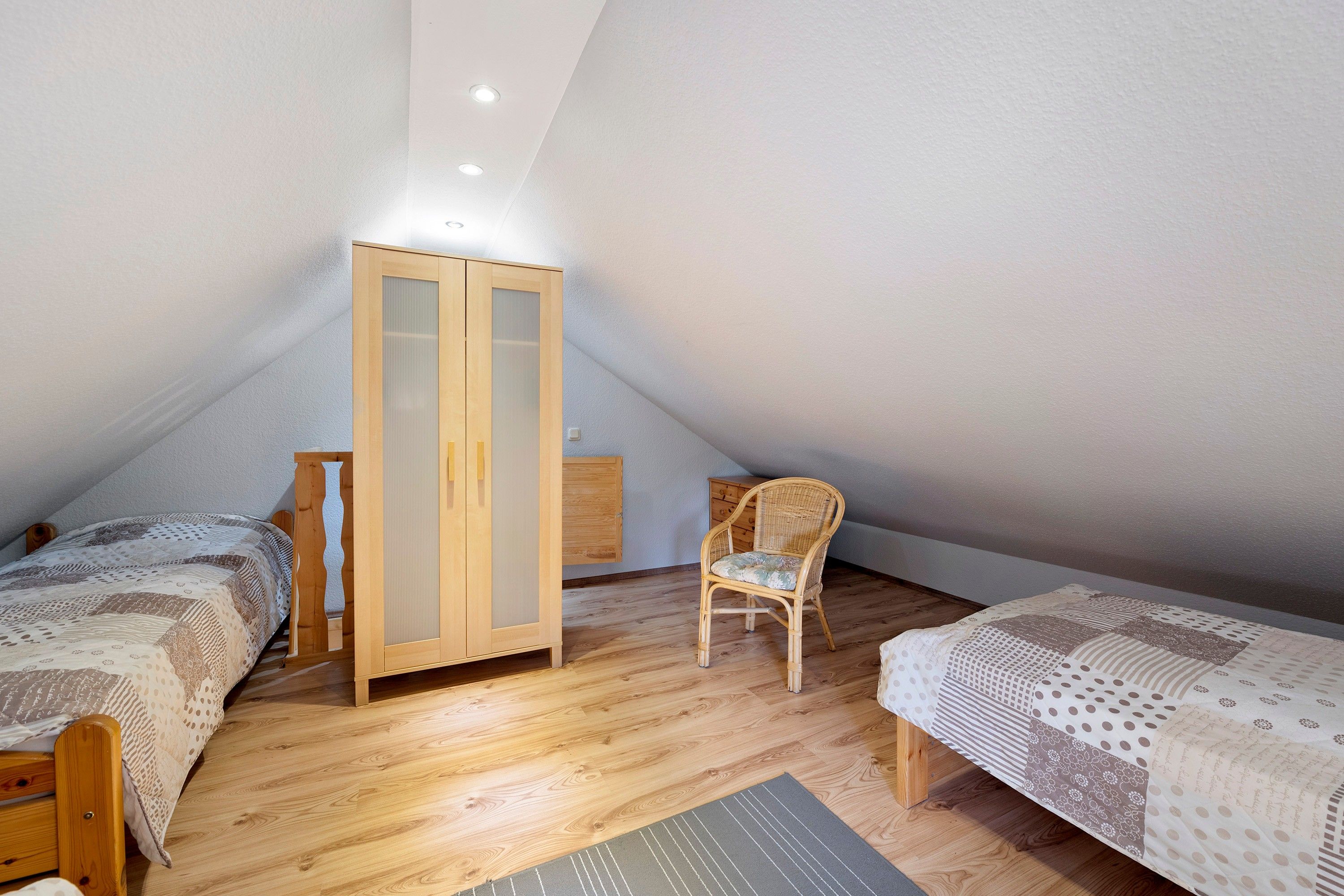 Ein Schlafzimmer mit zwei Holzbetten, einem Holzschrank, einem Korbstuhl und einem kleinen Holzschränkchen.