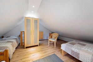 Une chambre à coucher avec deux lits en bois, une armoire en bois, une chaise en osier et une petite commode en bois.