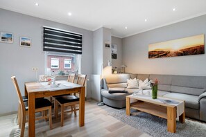 Ein modernes Wohnzimmer mit Essbereich, grauem Sofa und einem Gemälde eines Sonnenuntergangs.