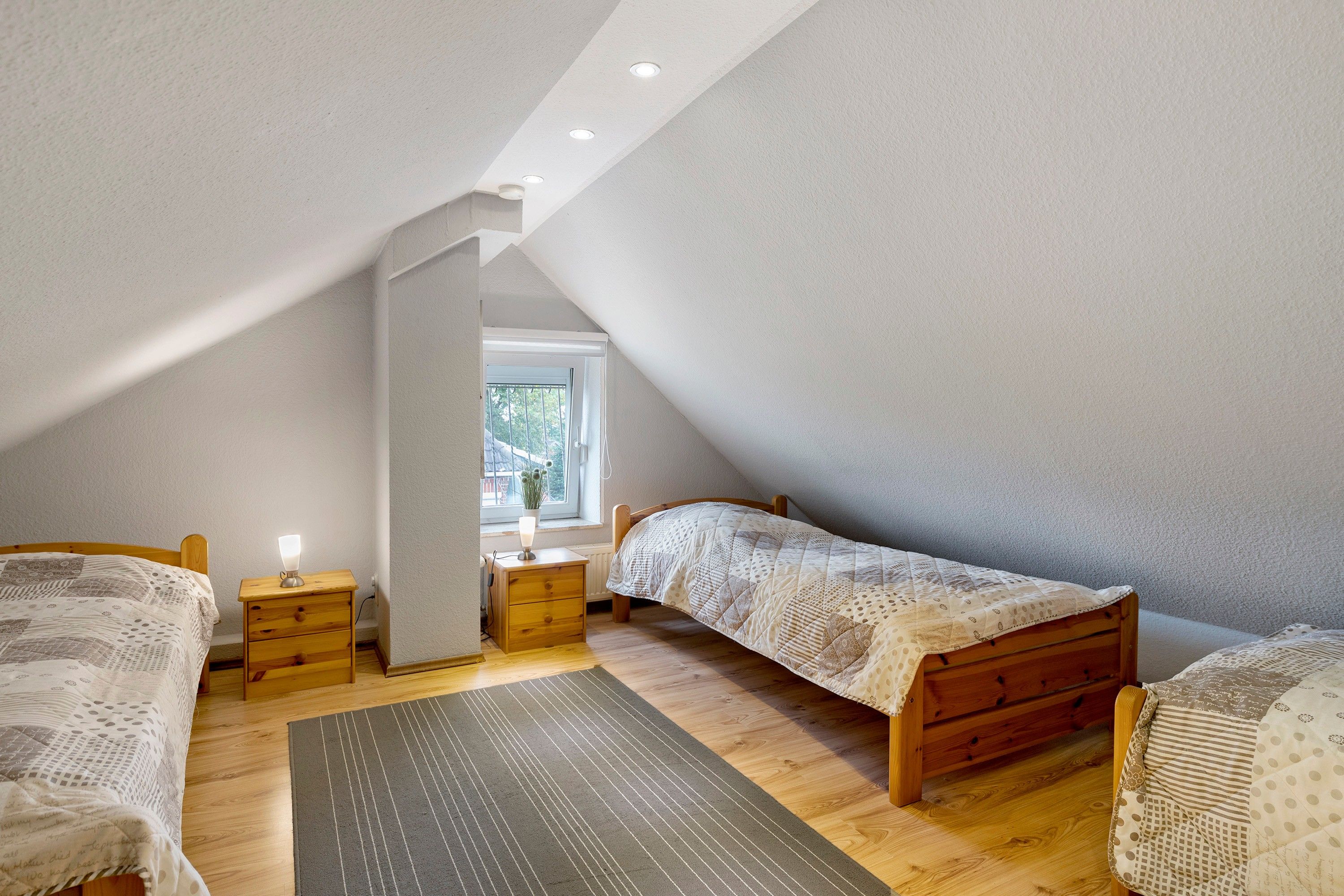 Ein Schlafzimmer mit zwei Einzelbetten, einem Nachttisch mit Lampe, einem Fenster mit Blick und einer schrägen Decke.