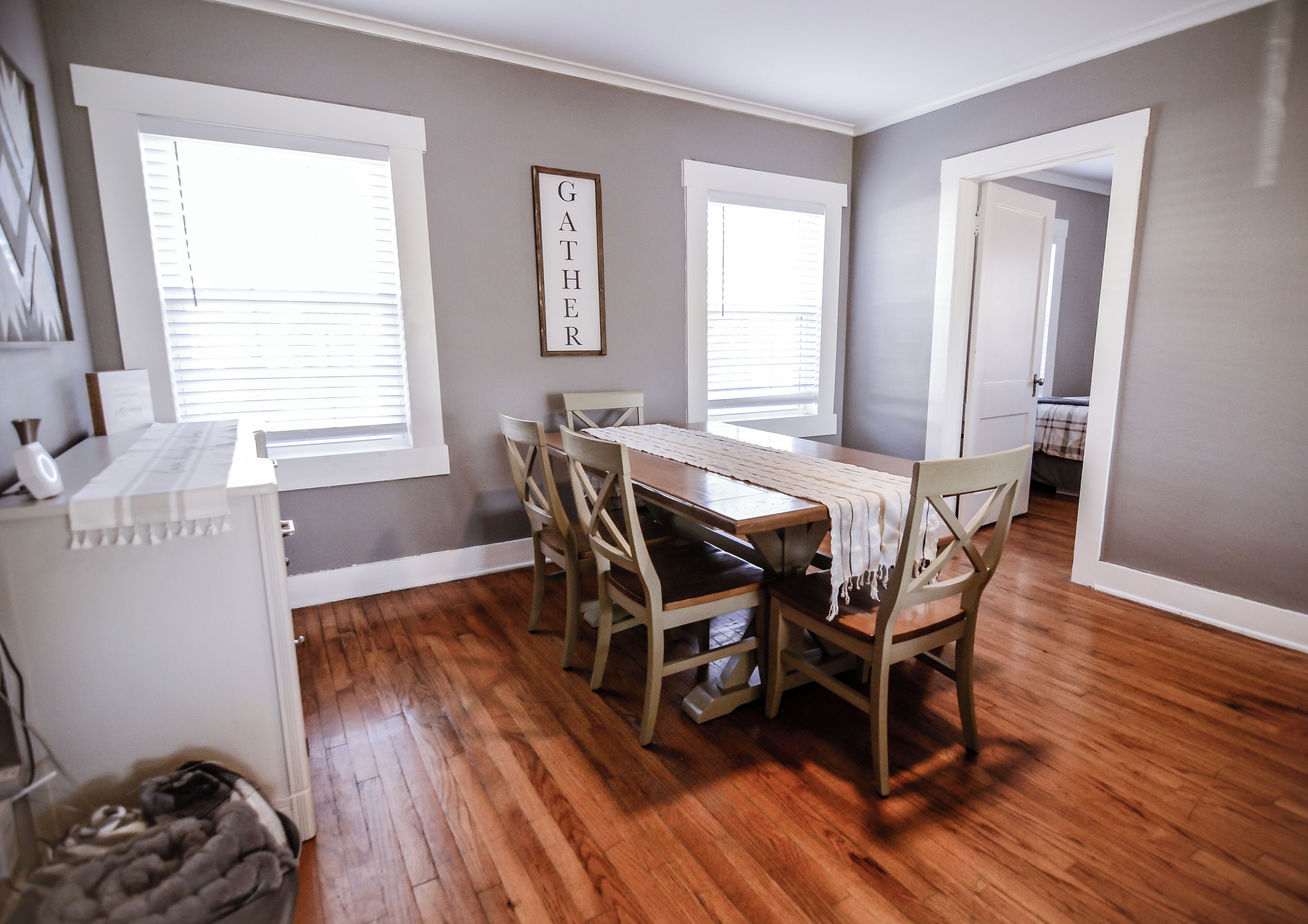 A dining area with a wooden table and chairs, a white cabinet, and a framed sign on the wall.