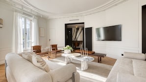 Un salón amplio con una mesa de centro de mármol, sofás, un televisor de pantalla plana y vistas a una escalera.