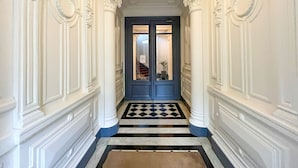 Un pasillo con molduras blancas ornamentales, una puerta azul con paneles de vidrio y un suelo a cuadros blanco y negro.