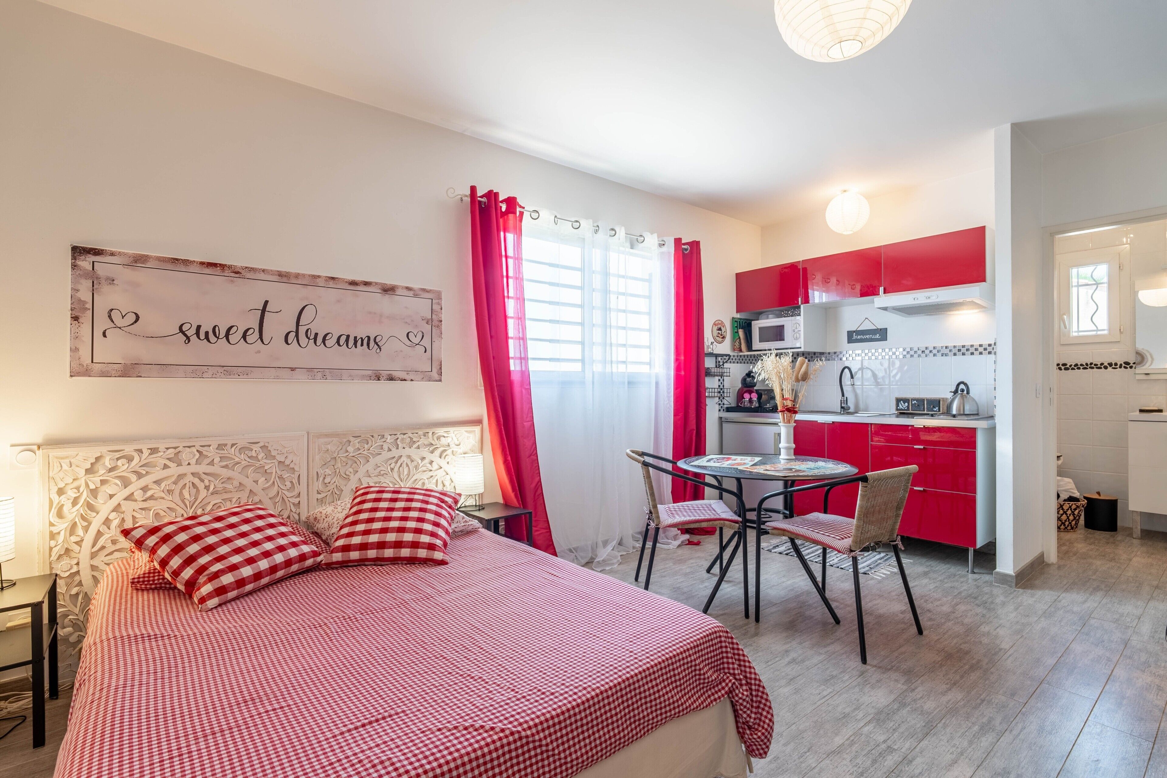 Un dormitorio con una cama, una mesita de noche, una colcha roja y blanca a cuadros, y un cartel en la pared.