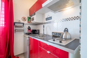 Une cuisine avec des placards rouges, un four à micro-ondes, une bouilloire et un évier.