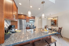A kitchen with granite countertops, stainless steel appliances, wooden cabinets, and pendant lighting. - SUMMER SALE! Charming studio with mountain views - Lahaina Shores 322 (Lahaina)