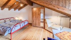 Una habitación con techo de madera, una cama con estructura metálica roja, un armario y un sofá.