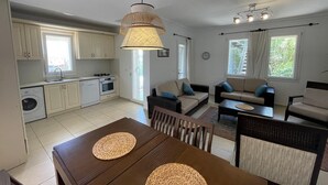 A modern kitchen with white cabinets, a dining table with woven placemats, and a living area with sofas and a coffee table.