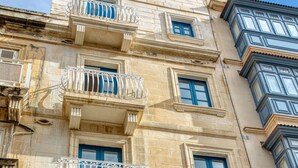 Un edificio de varios pisos con balcones, ventanas con contraventanas azules y un cielo despejado.