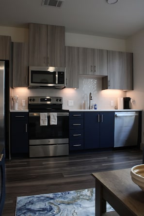 A modern kitchen with stainless steel appliances, dark cabinetry, and a wooden dining table.