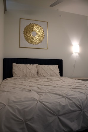 Un dormitorio con una cama, una lámpara fijada a la pared y una pieza decorativa enmarco.