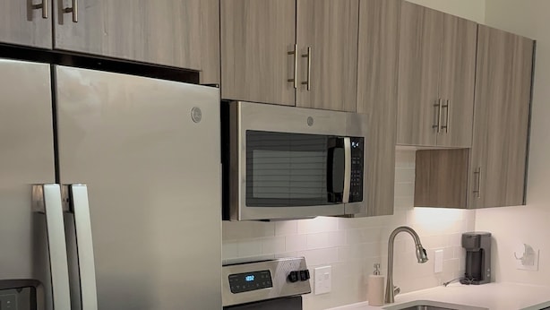 Una cocina moderna con electrodomésticos de acero inoxidable, armarios de madera, un microondas y un lavamanos.