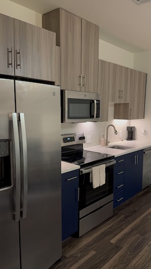 A modern kitchen with stainless steel appliances, wooden cabinets, a microwave, and a sink.