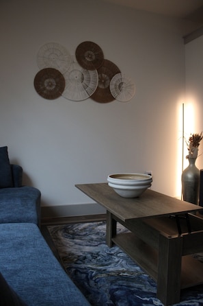 A modern living room with a sofa, a wooden table with a bowl, a vase with dried plants, and wall-mounted decorative items.