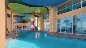An indoor swimming pool with a colorful water slide, a lifeguard tower, and a view of the ocean through large windows. - TWO GULF-FRONT MASTERS - BEST 2br in Splash, End Unit, Included Beach Chairs! (Panama City Beach)
