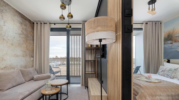 Ein modernes Hotelzimmer mit einer Couch, einem kleinen runden Tisch, einem großen Bett, einem Fernseher und einem großen Fenster mit Vorhängen.