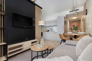 Una sala moderna con un televisor de pantalla plana, detalles de madera, un comedor con mesa y sillas, y una cocina al fondo.