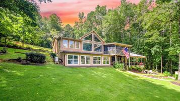 A two-story house with a large front lawn, a covered porch, and a flag.