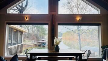 Une pièce dotée d’une grande fenêtre, d’un ventilateur de plafond, d’une table en bois et d’un vase rempli de fleurs.