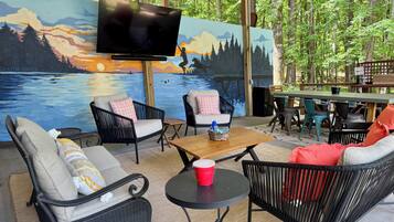An outdoor seating area with wicker furniture, a wooden table, and a mural of a sunset over water.