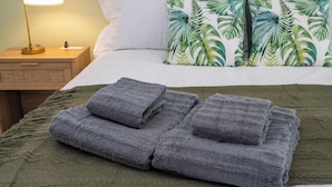 A neatly made bed with a green blanket, a pillow with a tropical leaf pattern, and a bedside lamp on a wooden nightstand. - Peaceful and cozy Botanic Retreat - FREE Shuttle (Orlando)