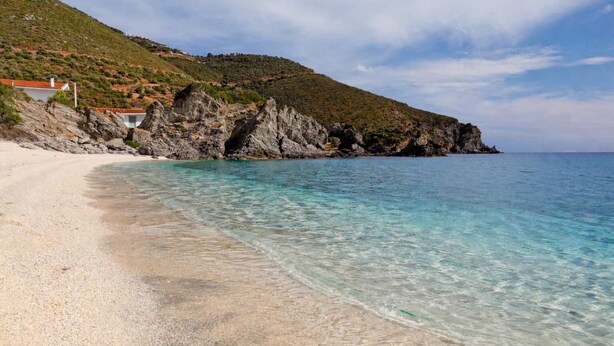 Una platja amb aigües turqueses cristal·lines, una riba sorrenca i penya-segats rocosos al fons.