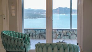 Habitació amb vista a un conjunt d'aigua i muntanyes, un balcó de pedra i una cadira amb textura.