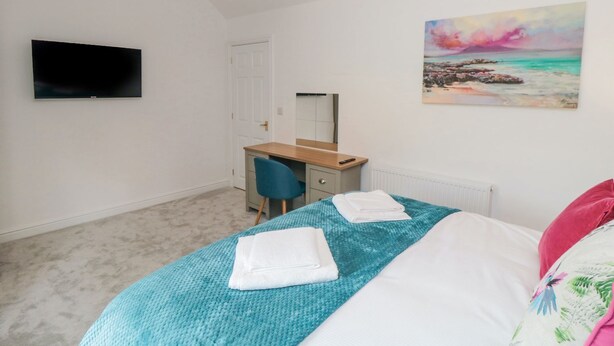 A bedroom with a bed, a desk, a chair, a television, and a painting on the wall. - Riverside House (Scarborough)