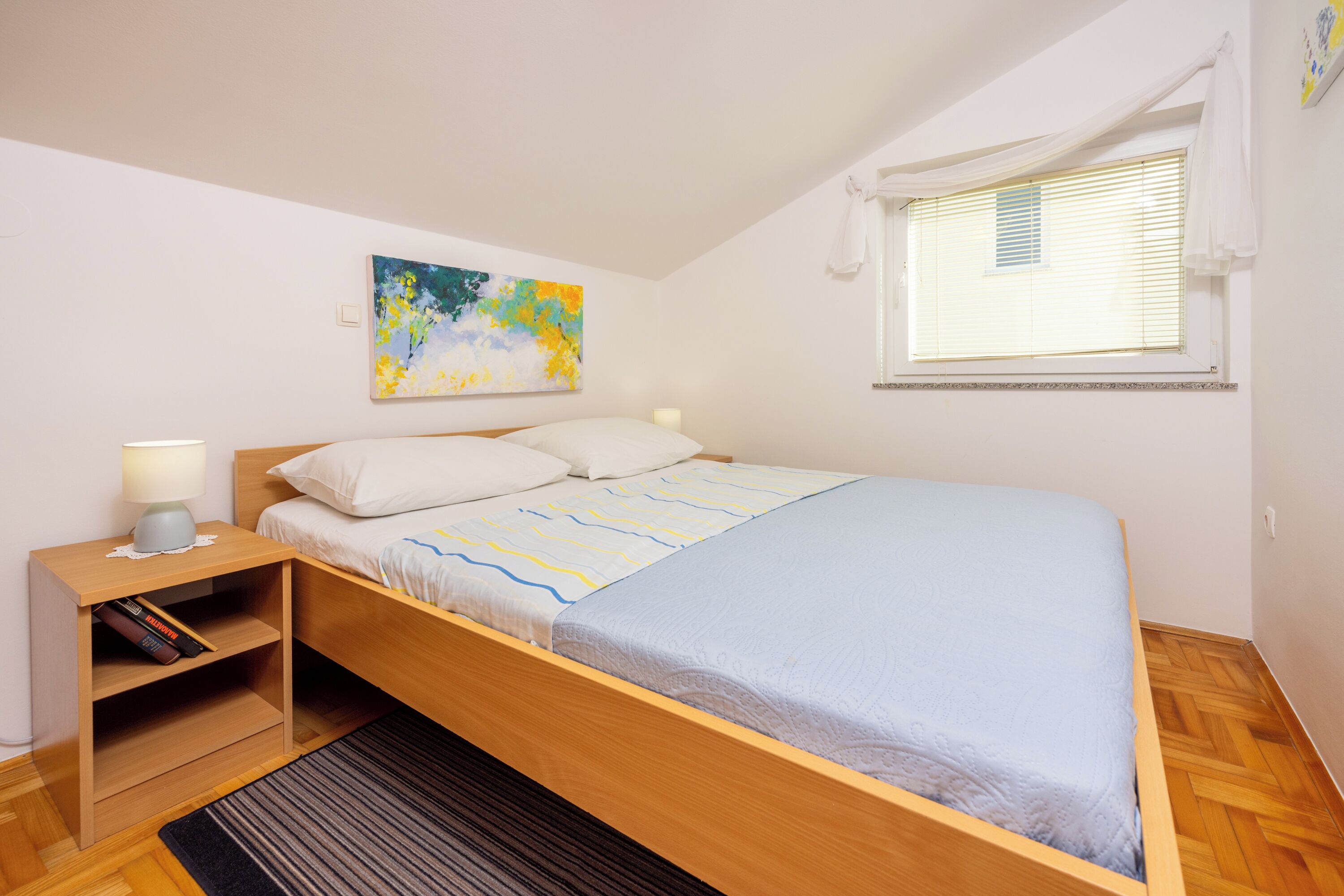 Une chambre à coucher avec un lit, une table de chevet, une lampe et une fenêtre avec des stores.