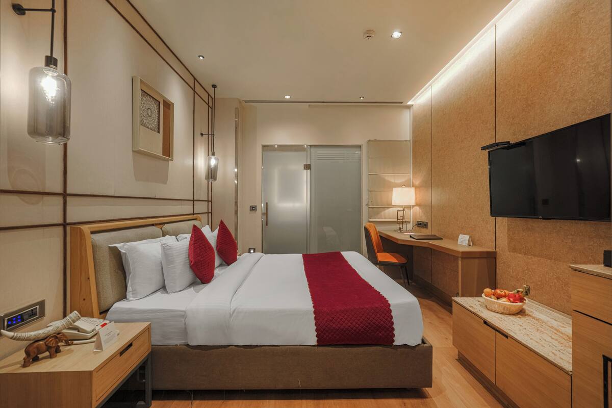 Habitación de hotel con cama, mesita de noche, lámpara, televisión y escritorio con silla.
