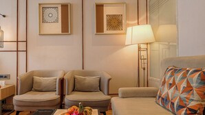 A hotel room with two armchairs, a sofa, a lamp, a wall-mounted artwork, and a fruit basket. - Ramee Collection Airport Road Mohali (Mohali)