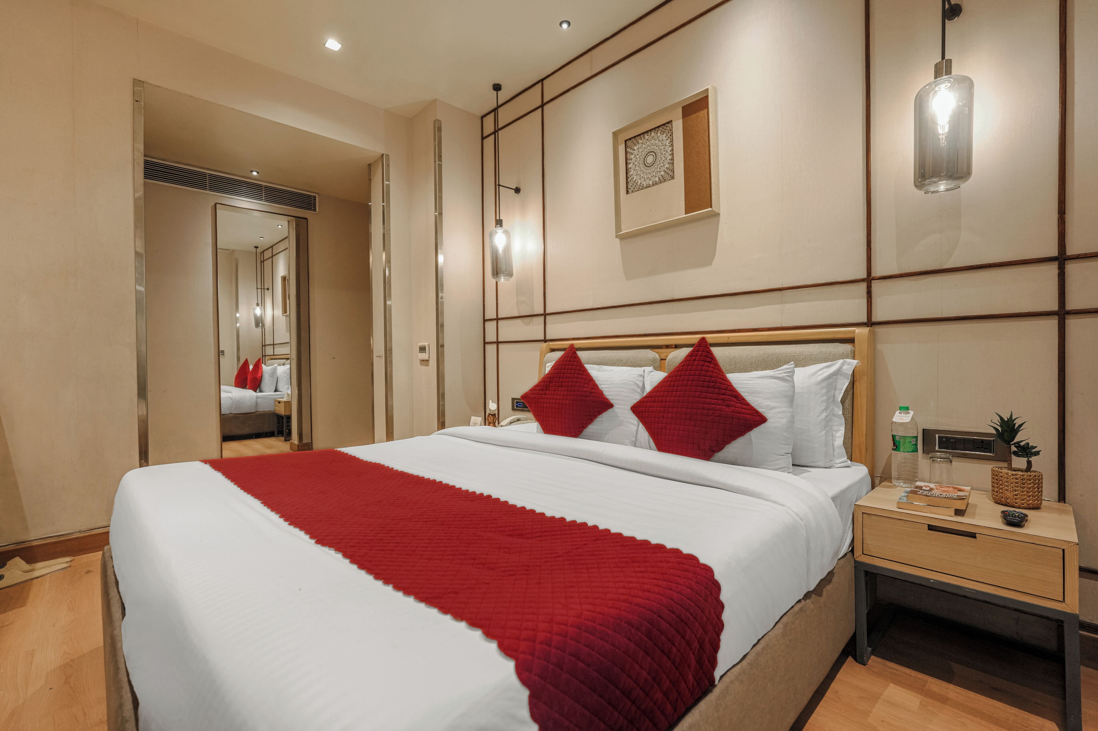 A hotel room with a large bed, a nightstand, a mirror, and a wall-mounted light fixture.