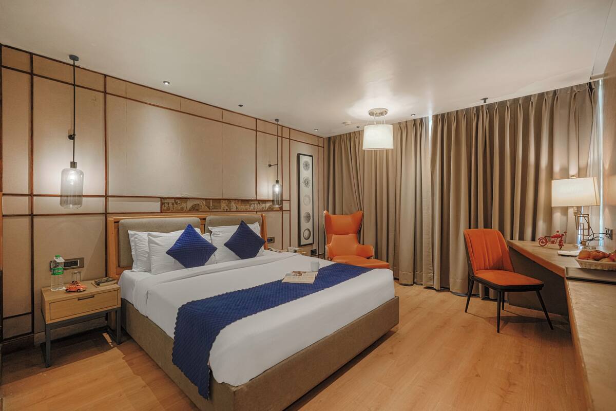 Habitación de hotel con una cama grande, un escritorio con lámpara, una silla y una mesita de noche con una botella y un coche de juguete.