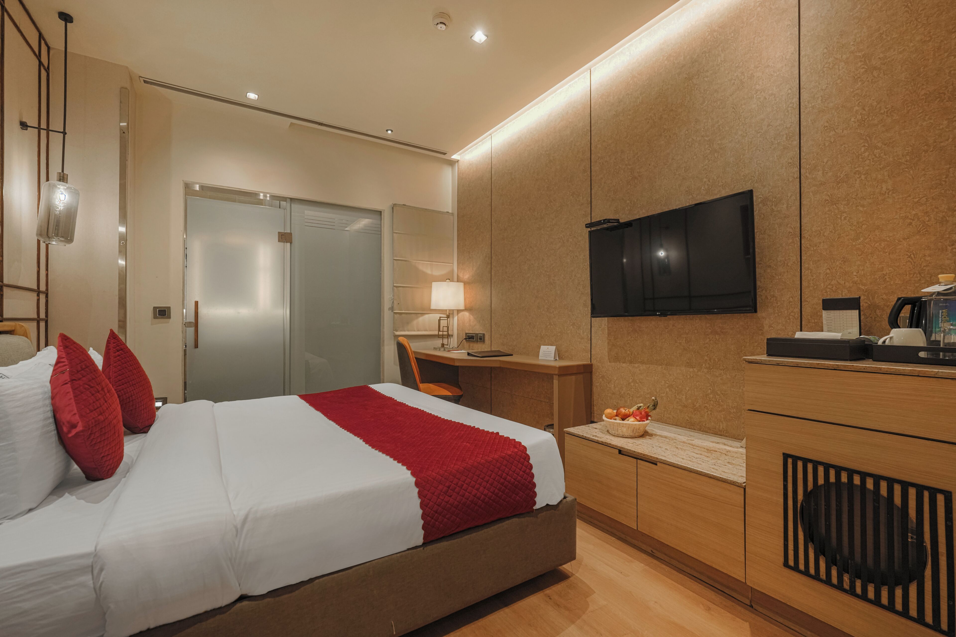 A modern hotel room with a bed, desk, television, and a small kitchenette area.
