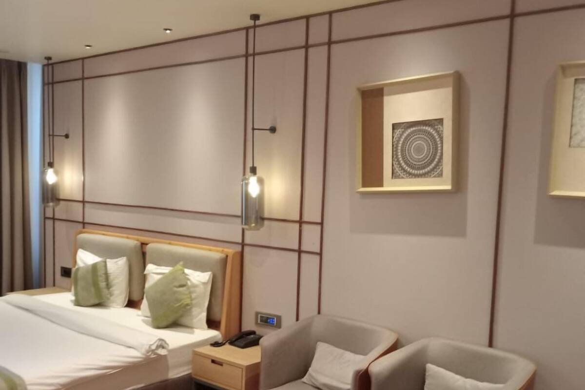 Una habitación de hotel con una cama, dos sillones, una mesa de centro y una mesita de noche con lámpara.
