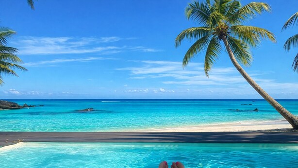 Une vue sur la piscine, avec une eau turquoise cristalline, une plage de sable et des palmiers.